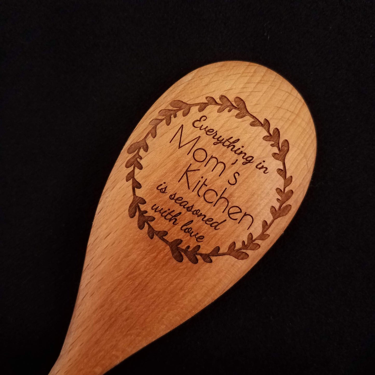 Customizable beech wood spoon laser engraved with Everything in Mom's Kitchen is Seasoned with Love inside a rustic wreath